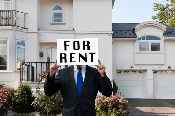 Man holding a "FOR RENT" sign in front of a big house