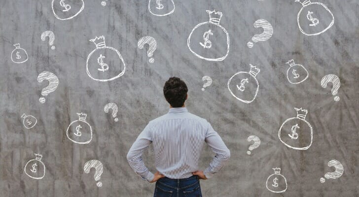 Man standing in front of chalkboard with drawings of money bags and question marks
