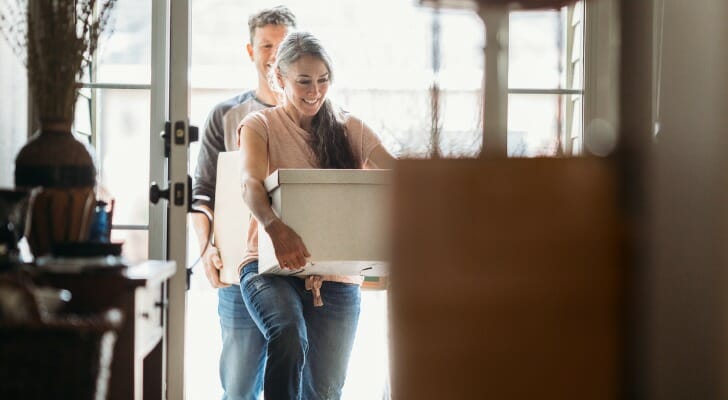 Image shows two adults carrying moving boxes into a new home. SmartAsset analyzed data on various factors to find the cities where the average household can afford the most and least home.