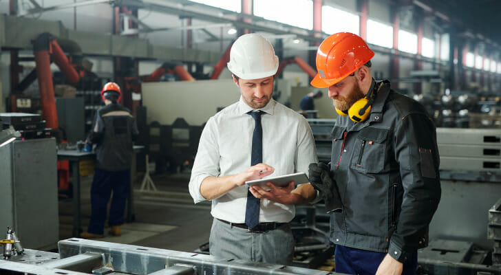 Image shows two workers wearing hard hats standing next to each other to consult a document in their workplace. SmartAsset analyzed data on income growth, job growth, manufacturing workforce and unemployment to find the best places to work in manufacturing.