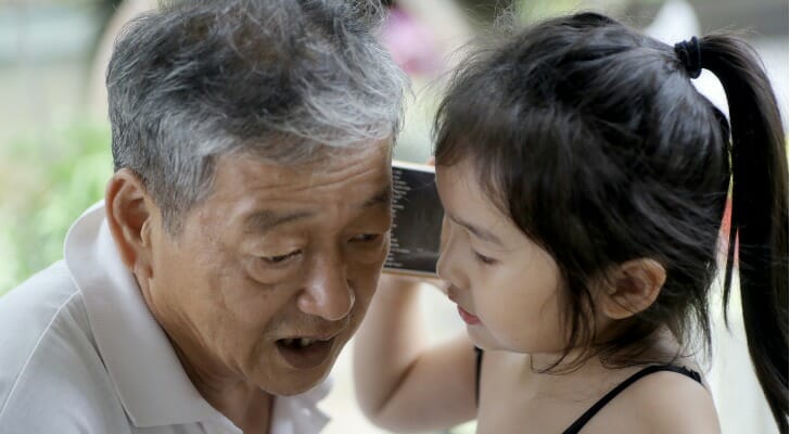 Grandfather and granddaughter listening to the same smartphone