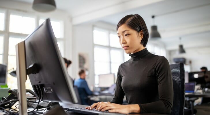Image shows a woman tech worker at her desk working at a computer. SmartAsset analyzed various data points to conduct its latest study on the best cities for women in tech.
