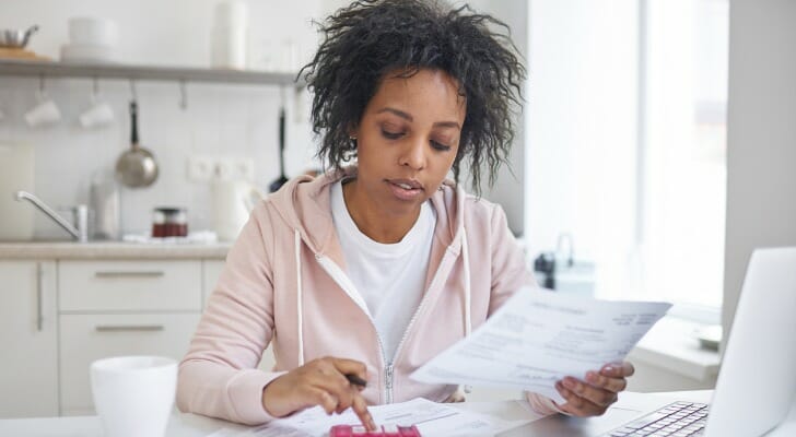 Image shows a woman sitting at a table with a calculator and bills in front of her; she is squaring away her latest financial statements. SmartAsset analyzed various data to identify where Americans are most and least financially literate. 