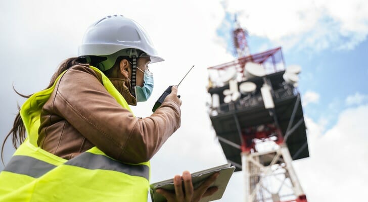 Image shows an engineering wearing a hard hat and a protective face mask working near a telecommunications tower. SmartAsset analyzed various data sources to identify the states with the best infrastructure.