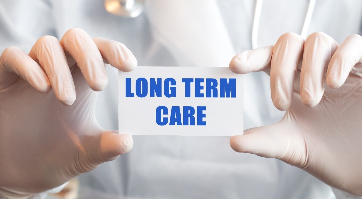 Image shows a medical worker's gloved hands holding a card that reads, "Long Term Care."