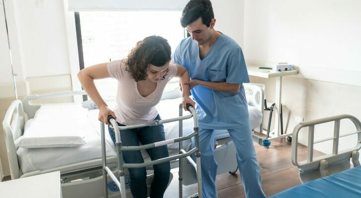 Image shows a nurse helping someone get up to use a walker after being injured. Short-term care insurance may be able to help cover costs for a service like this.