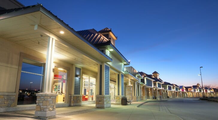 Image shows a strip mall at night. Strip malls remain a solid investment, either through direct purchase or investing in a real estate investment trust (REIT). 