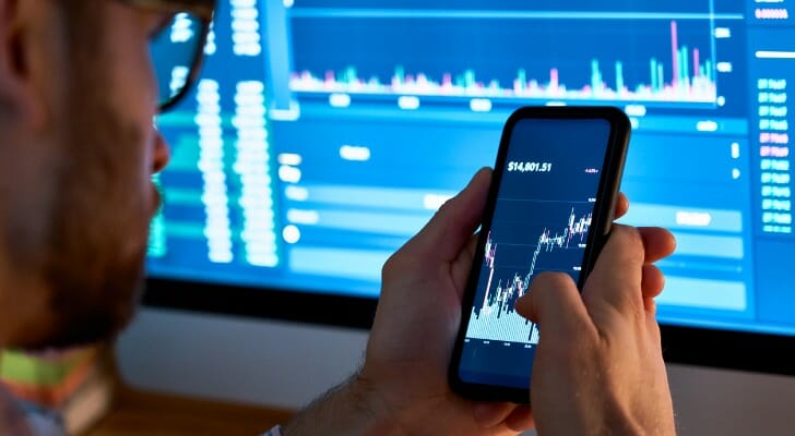 An investor monitors a stock on his smart phone. A Natixis Investment Managers survey of 500 institutional investors around the world identified the sectors and classes expected to post the biggest gains in 2022. 