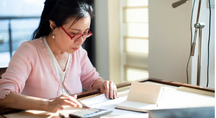 A retired woman works on her finances at her table. J.P. Morgan has developed precise income replacement targets for retirees based on their pre-retirement income. 