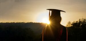 A silhouette with wearing a graduation cap looks into the horizon.