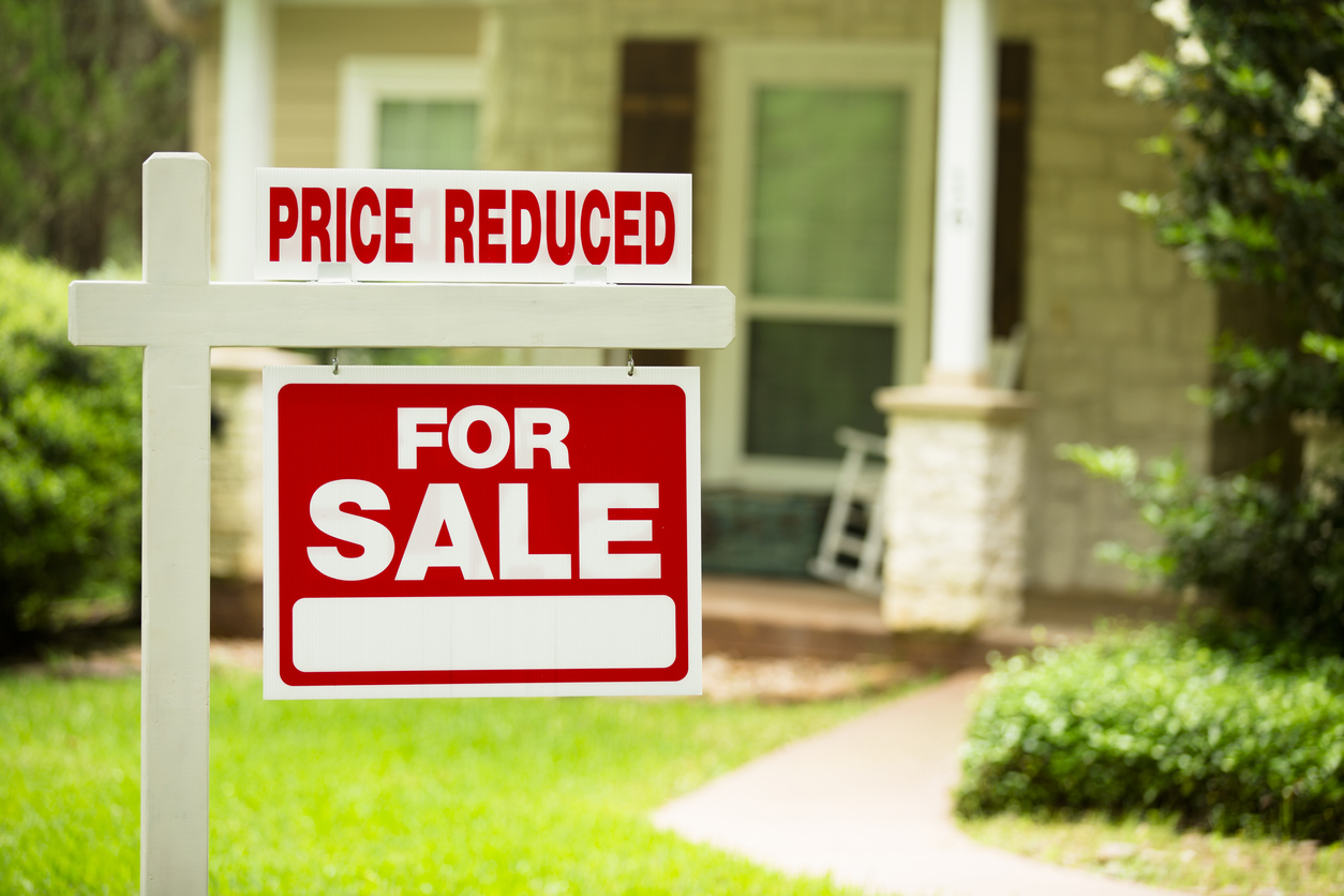 A "For Sale" sign outside a house with a "Price Reduced" attachment