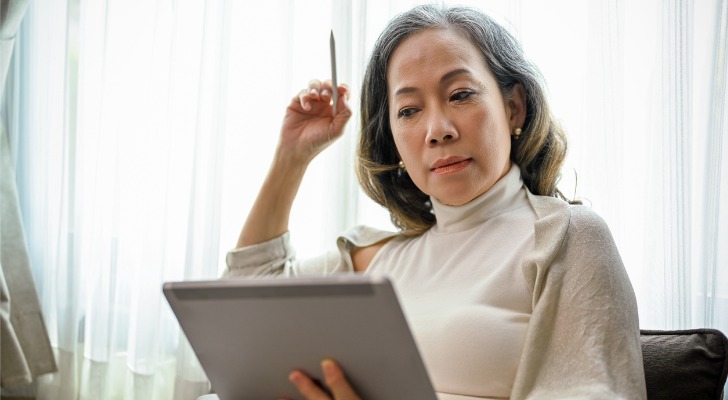 A woman who's approaching retirement age looks over her 401(k) account on a tablet.