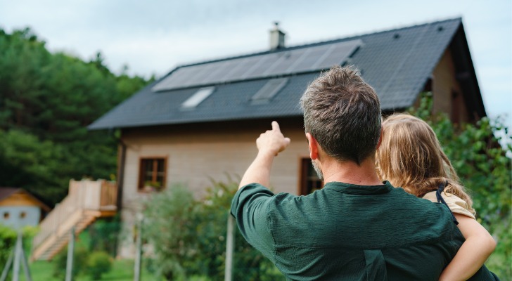 A father points to the solar panels on his family home and explains how they work to his daughter.
