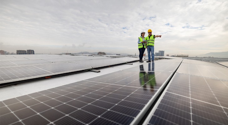 A pair of engineers look over a series of solar panels on the roof of a building.