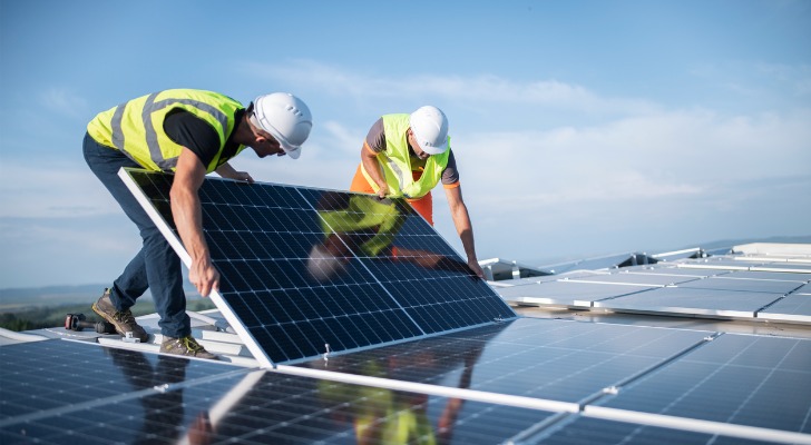 A pair of engineers install a solar panel on the roof of a building.
