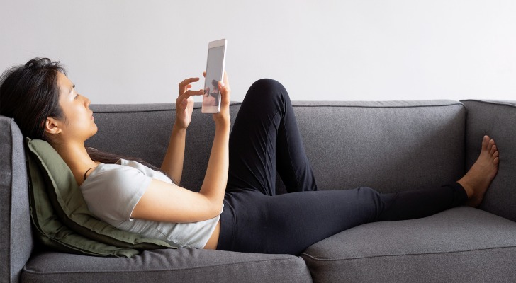 A woman looks over ETFs to potentially investing while lying on her couch. 