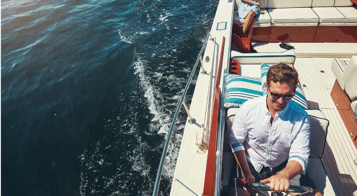 An ultra-high-net-worth individual at the helm of his yacht while his wife relaxes in the background.