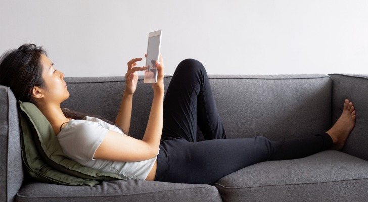 A woman lies on her couch and looks over different types of ETFs for her portfolio.