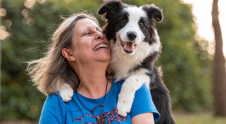 A 62-year-old retiree smiles as her dog jumps on to her back. 