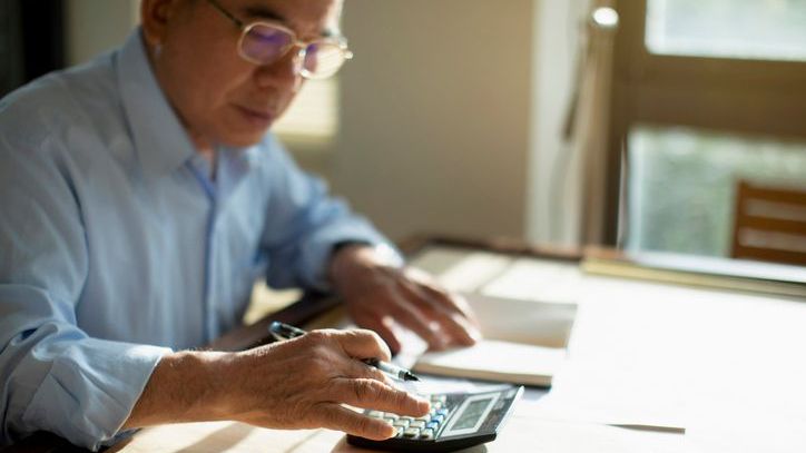 A man adds up his monthly expenses on a calculator as he estimates how long his savings may last in retirement.