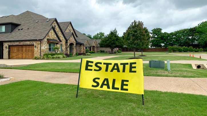 A sign for an estate sale is set up on a lawn.