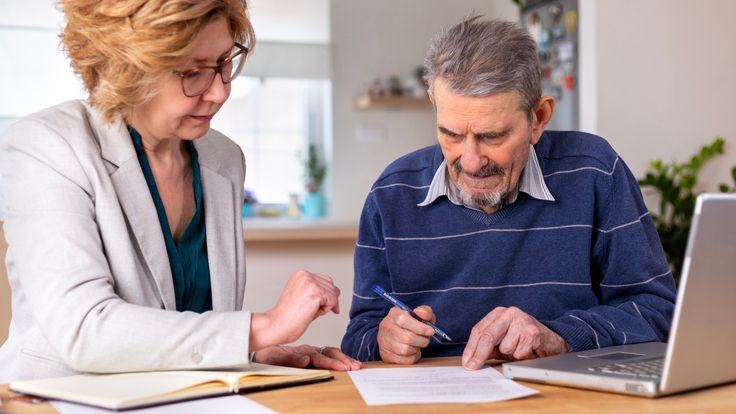 A man signs paperwork giving his friend on the left power of attorney. 