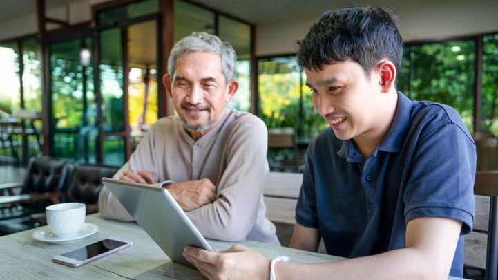 A man looks online at properties to purchase with the help of his father. 