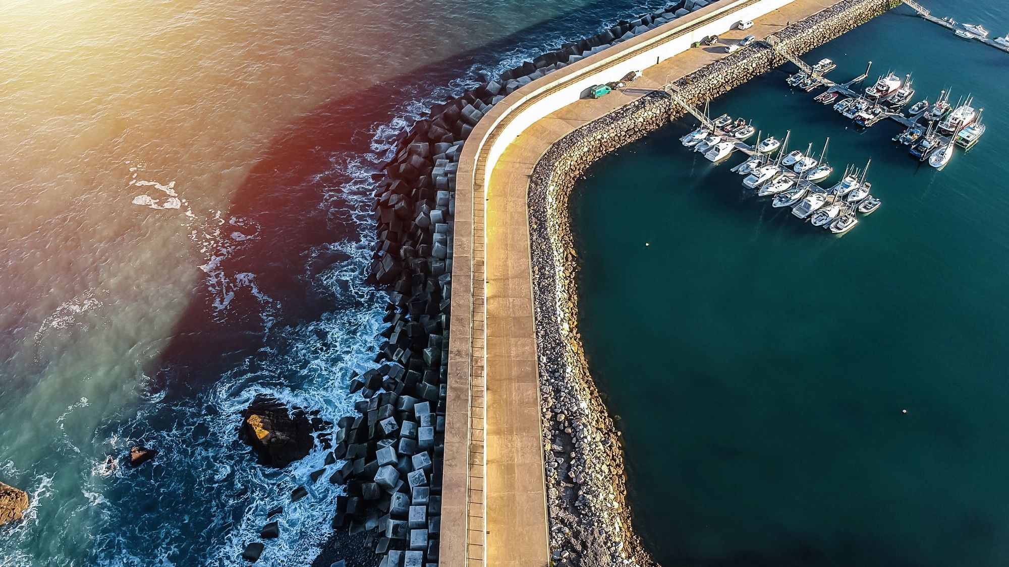 A wall protects a harbor and its docked boats from the rough waters of the sea. 