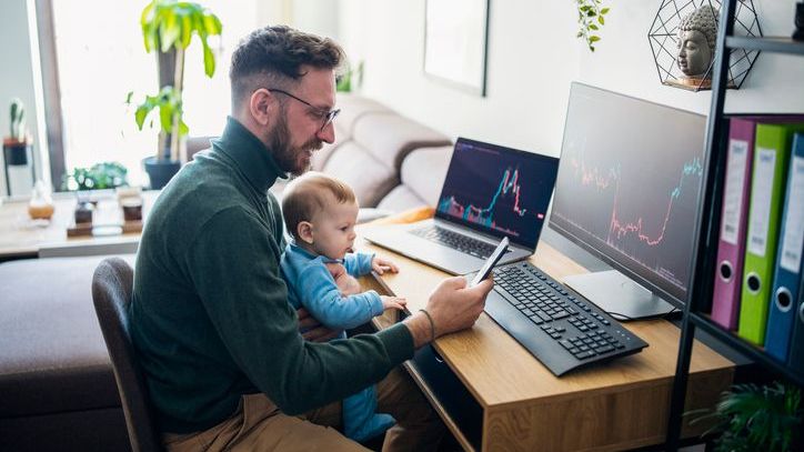 A father looks over his portfolio of exchange-traded funds (ETFs) while holding his infant son.