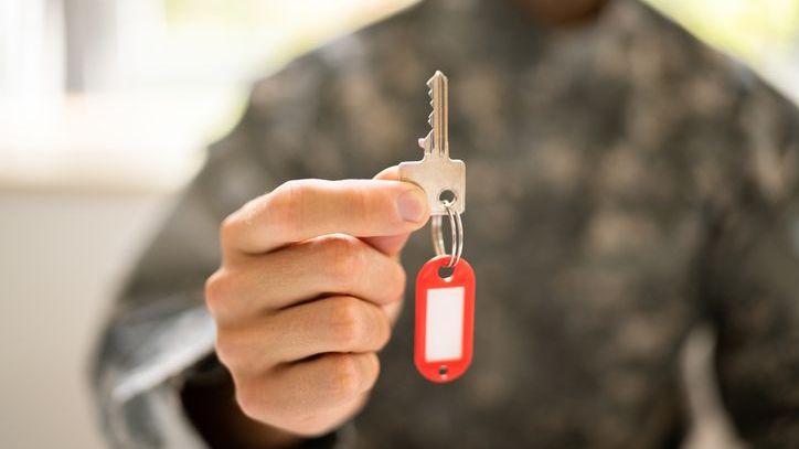 A soldier in fatigues holds out the key to his new home, which he bought with a VA loan.