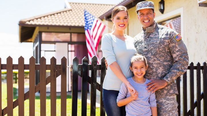 A member of the military stands with his wife and daughter outside of the home they purchased using a VA loan.