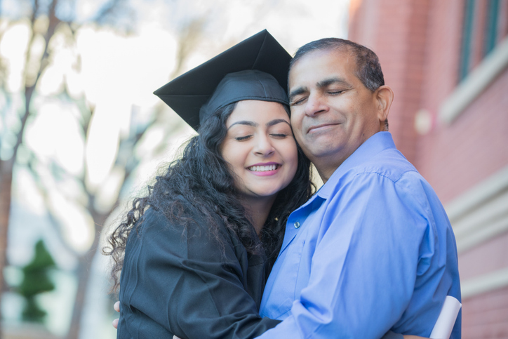 A college graduate hugs her father on graduation day. 