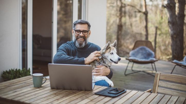 A man pets his dog while reviewing his financial plan for retirement.