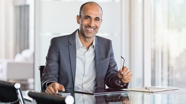 A financial manager sits and smiles behind his desk.