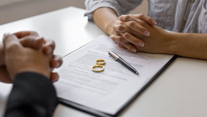 A divorcing couple sits across from each other while discussing their agreement.