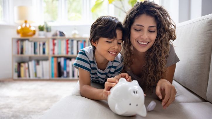 A woman watches her son open his piggy bank.
