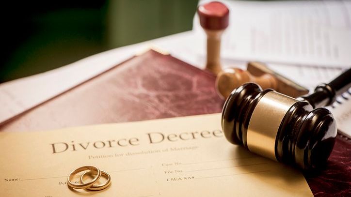 A pair of wedding bands and a gavel sit on top of a divorce decree. 