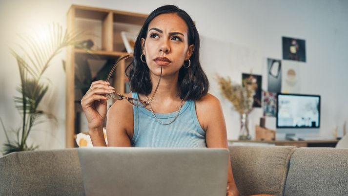 A woman looks over her portfolio on her laptop and contemplates whether she's let confirmation bias impact her investment decisions.