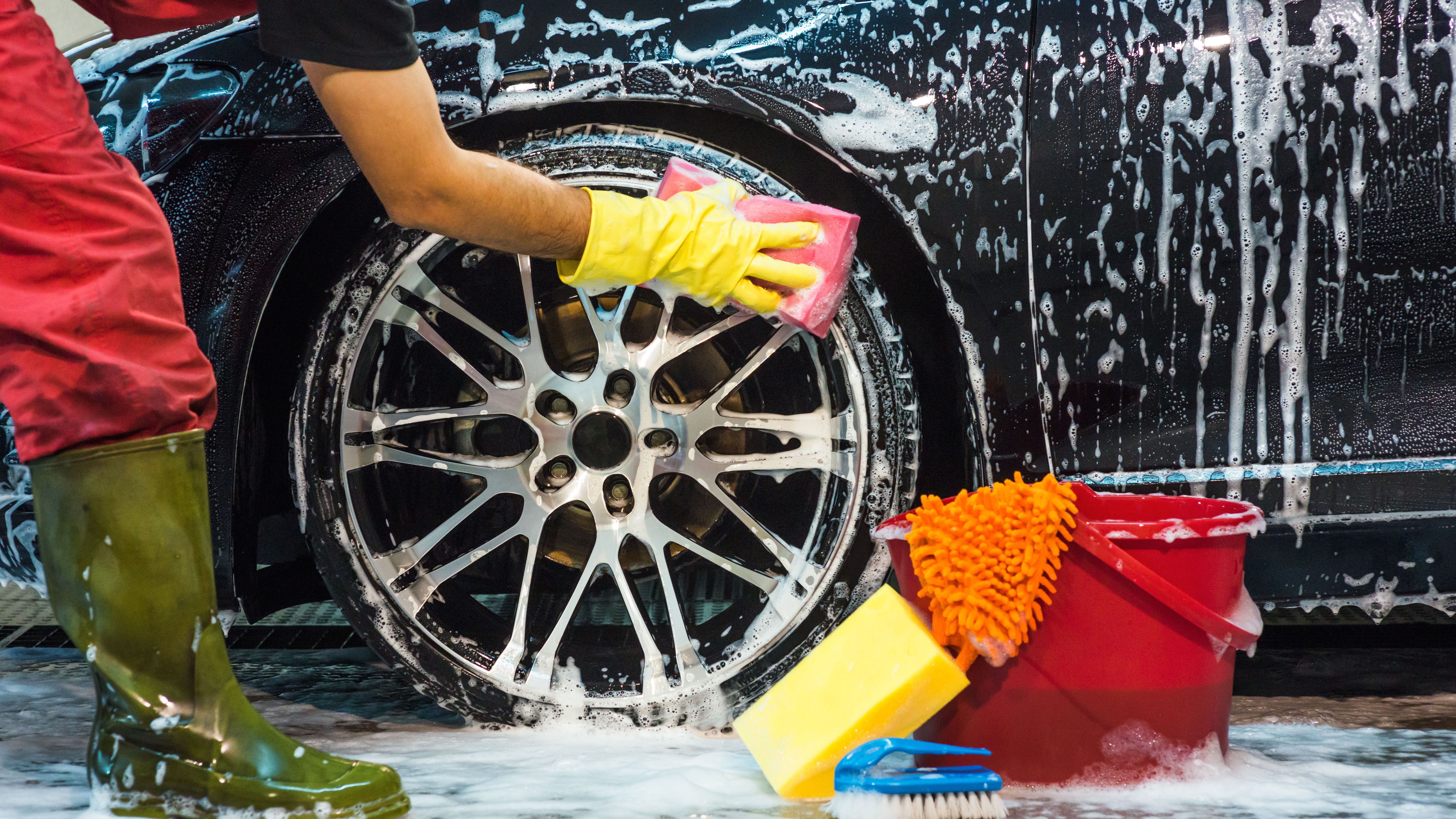 A car wash employee scrubs the rims of a car. 