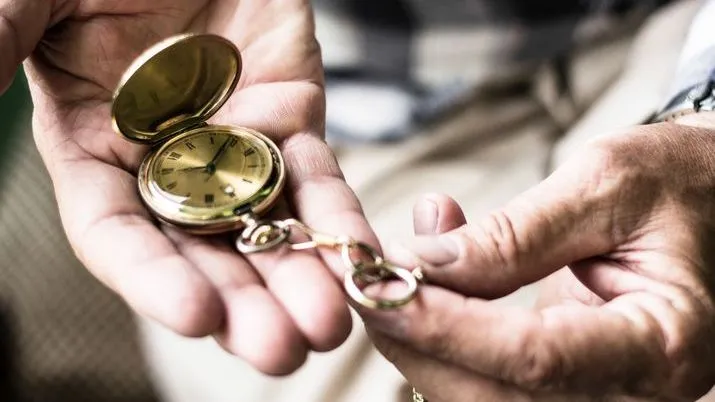 A man holds an antique timepiece in his hands.