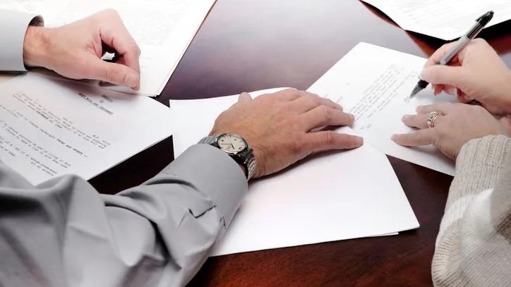 A woman signs a codicil while sitting next to another person.