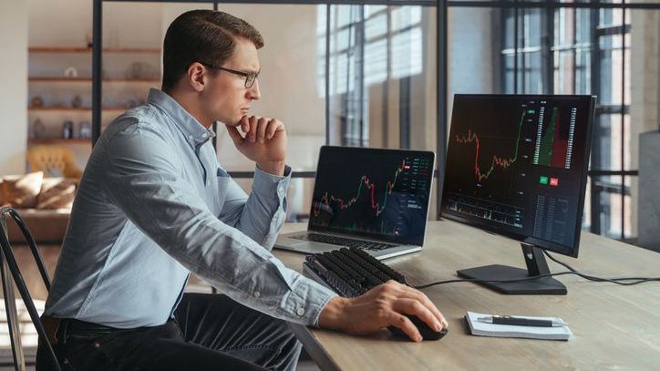 A man looks over price charts on two computer monitors. 
