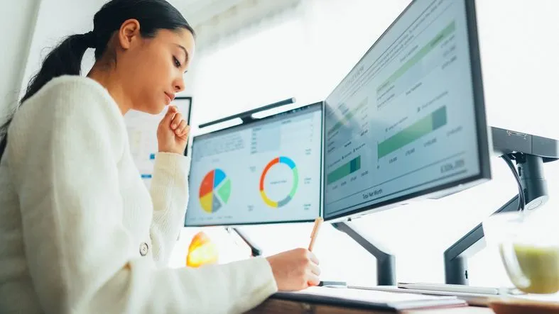 A woman works in front of two computer monitors.