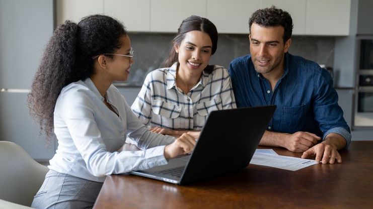 A woman points to her laptop screen while a man and woman look on. 