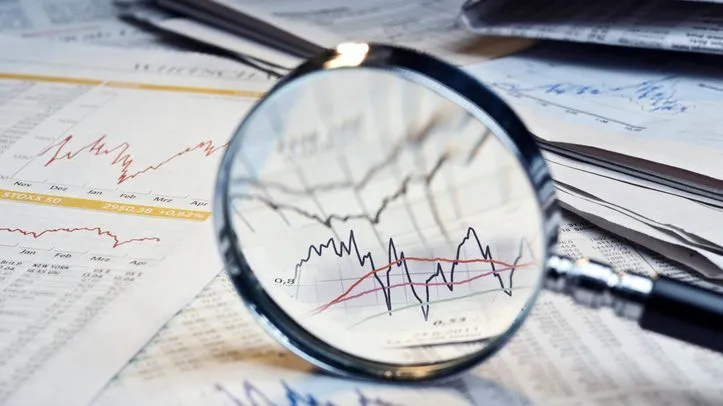 A magnifying glass and newspapers with exchange rate tables and diagrams.