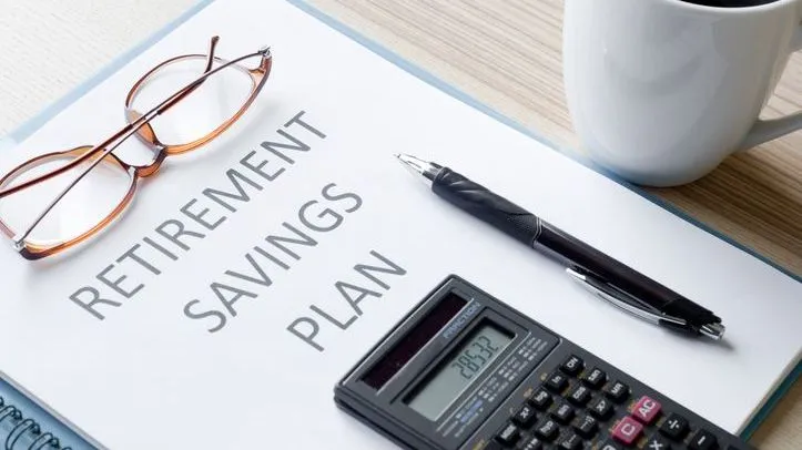 A pair of glasses, a pen and a calculator all rest on top of  retirement savings plan documents.