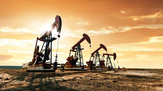 A series of four oil derricks pump oil on a desert property. 