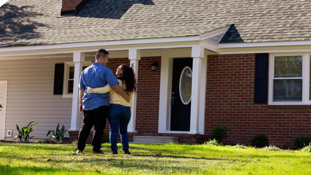 A young couple stands in front of their new home.