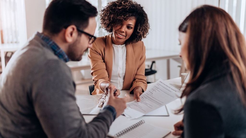 A couple signing loan agreement in front of a bank representative. 