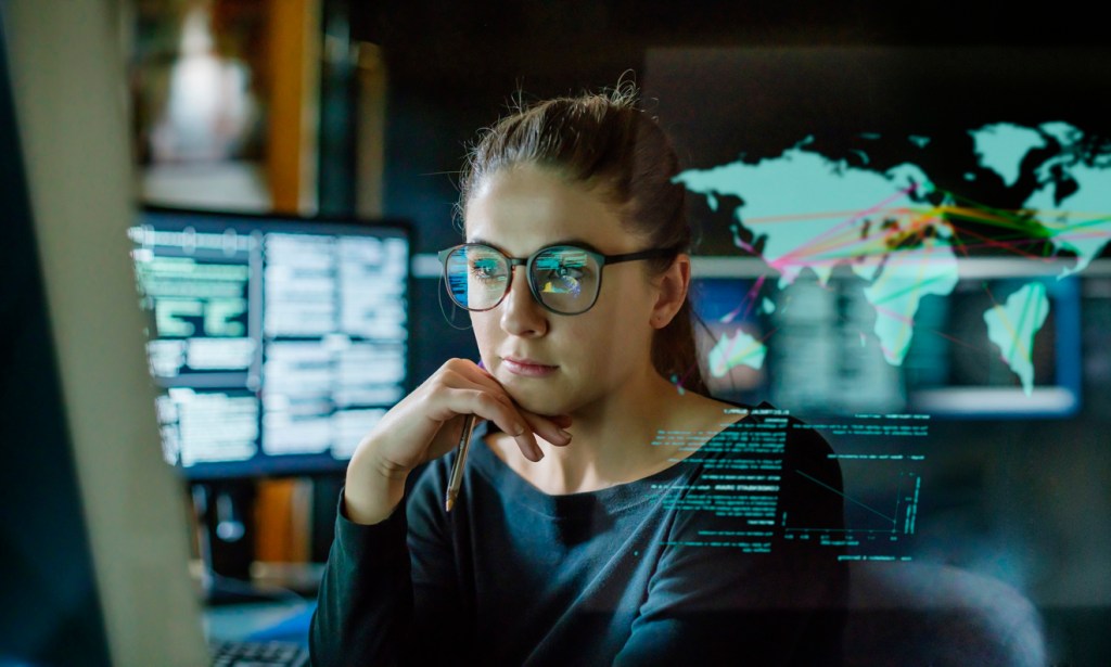 A woman is surrounded by computer monitors in a dark office.